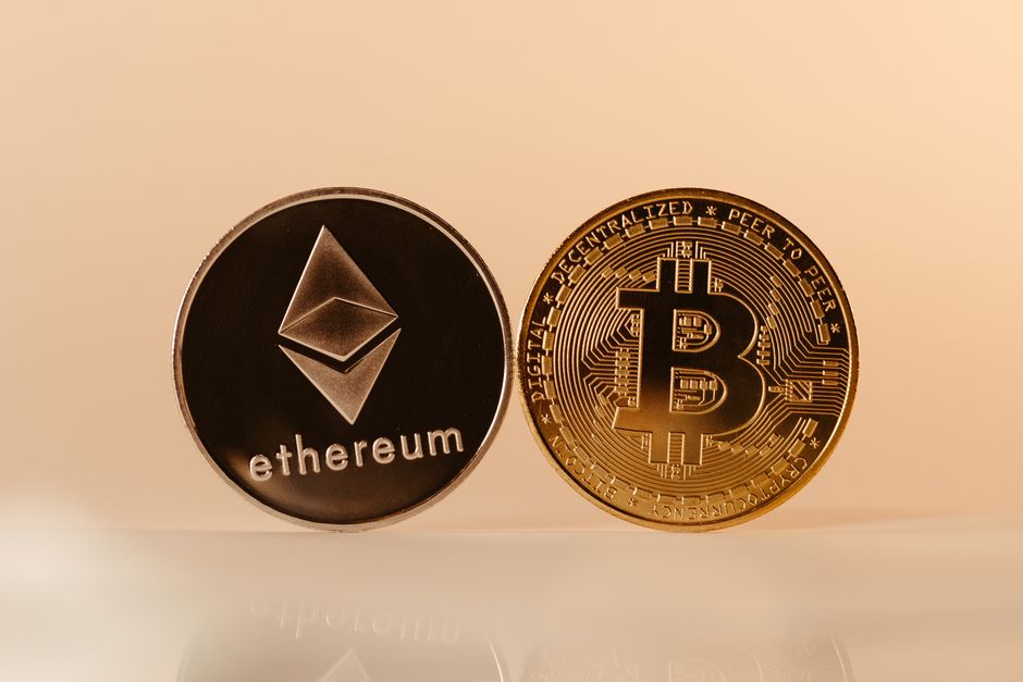 Close-up depiction of the gold-colored Bitcoin logo alongside the silver-colored Ethereum logo against a digital network map. Close-up depiction of the gold-colored Bitcoin logo alongside the silver-colored Ethereum logo against a digital network map.