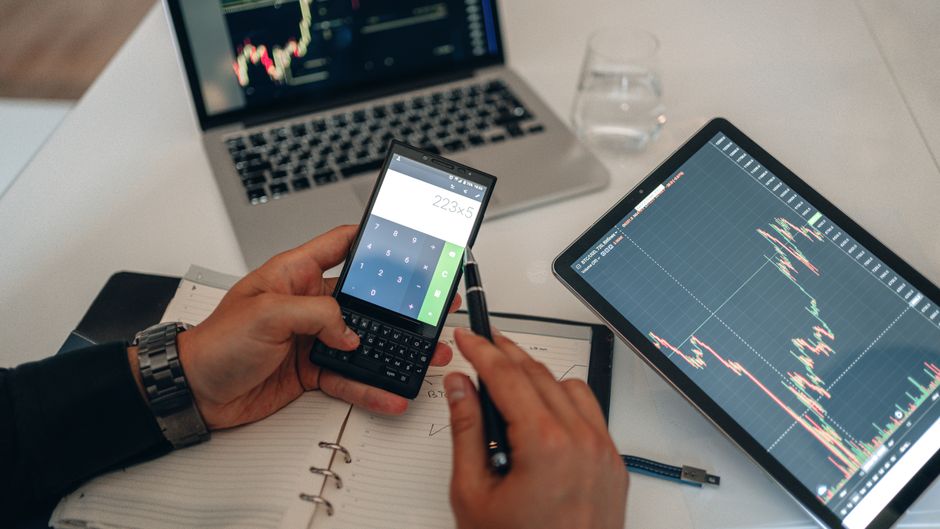 A professional financial calculator sitting next to a notebook with handwritten trading notes and a tablet computer. A professional financial calculator sitting next to a notebook with handwritten trading notes and a tablet computer.